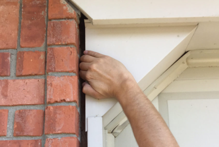 man sticking hand in door gaps on brick home